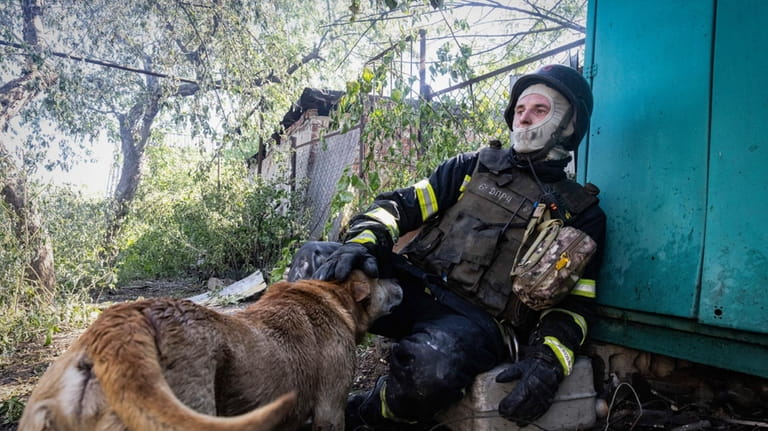 A firefighter pets a dog as he rests after putting...