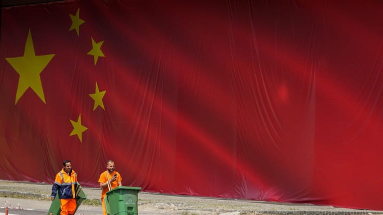 Cleaners walk in front of a Chinese national flag placed...