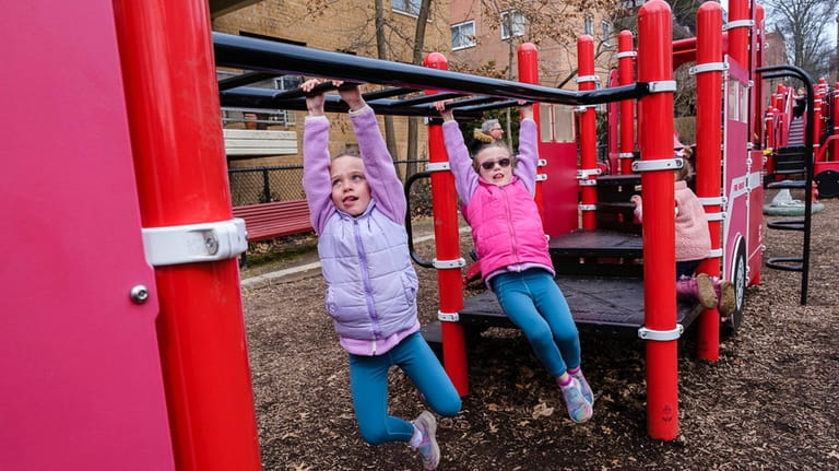 Twins Charlotte and Ellie Traina swing between ladder rungs at...