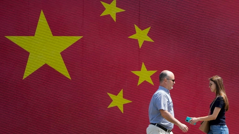 People walk in front of a Chinese national flag in...
