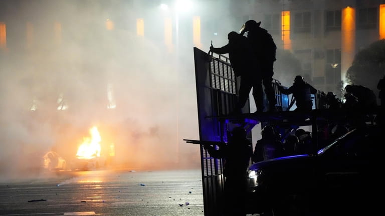 A police car on fire as riot police prepare to...