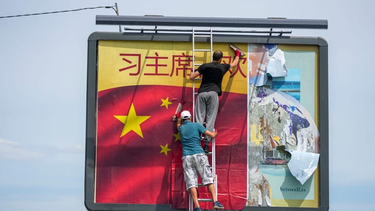 Workers stick a Chinese national flag on a billboard in...