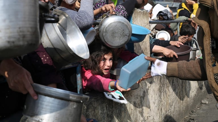 Palestinians line up for free food during the ongoing Israeli...