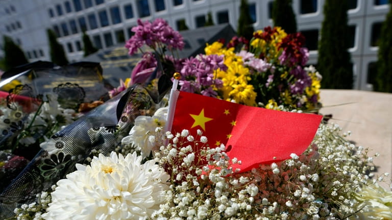 A Chinese flag is placed near flowers on a monument...