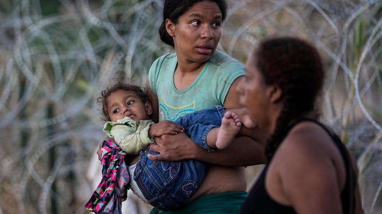 A woman carries her child after she and other migrants...