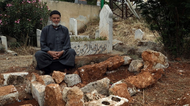 Mohammed Hassan Masto sits next to the grave of his...