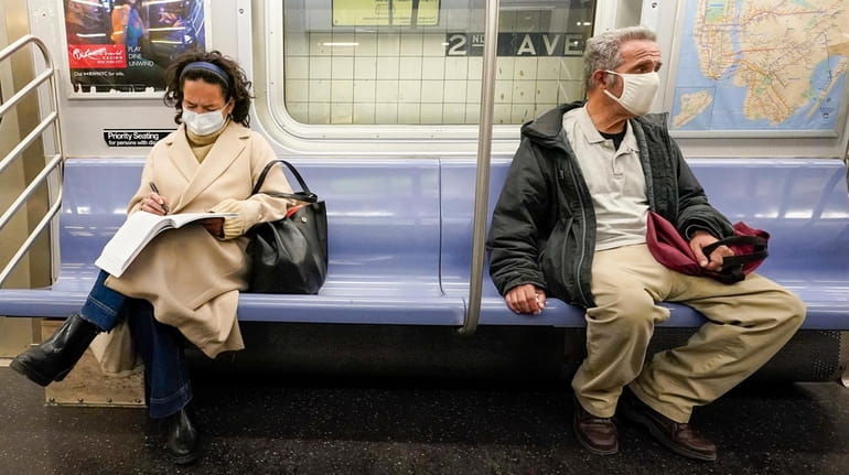 Commuters wear masks and social distance while riding an M...