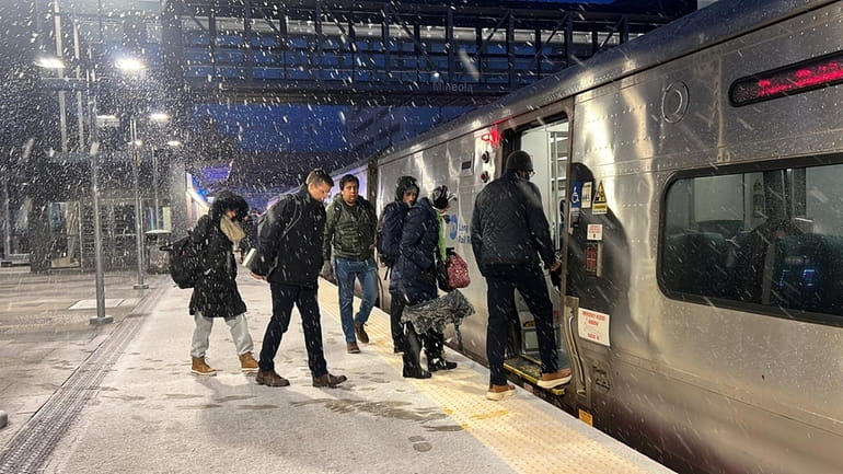 Commuters board the train at the Mineola LIRR station as snow...