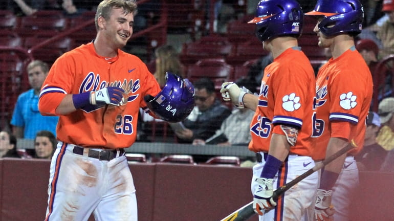 Clemson's Reed Rohlman, left, returns to the dugout after scoring...