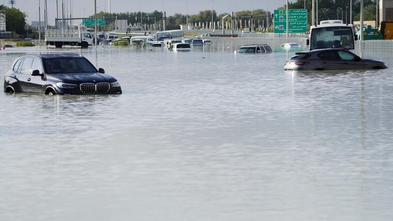 Vehicles sit abandoned in floodwaters covering a road in Dubai,...