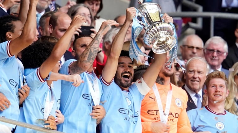Manchester City's Ilkay Gundogan, center, holds up the winners trophy...