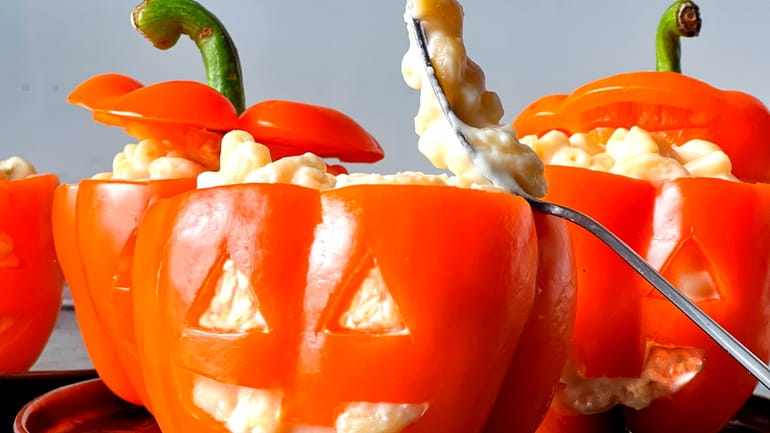 Orange peppers carved with jack-o-lantern faces are filled with Mac...