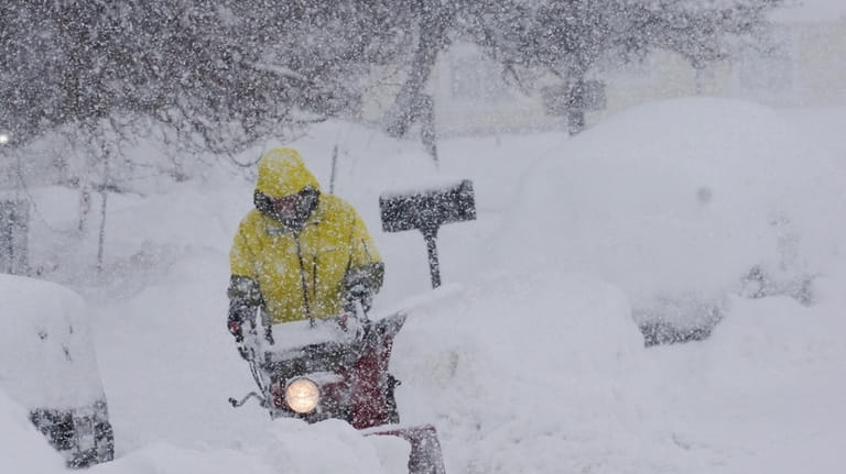 A person uses a blower to clear snow during a...