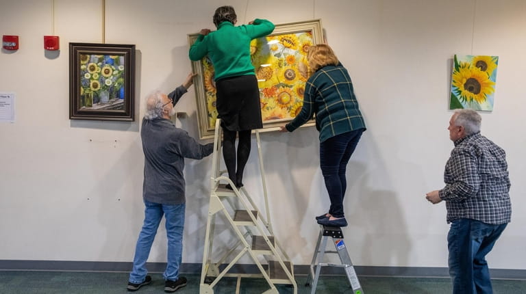 Volunteers hang one of the paintings made by about 50 artists participating...