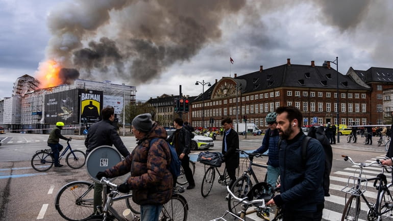 People ride bicycles as smoke rises from the Old Stock...