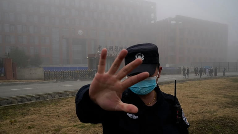 A security person moves journalists away from the Wuhan Institute...