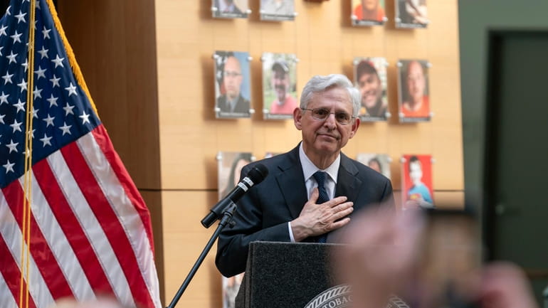 Attorney General Merrick Garland speaks next to a wall with...