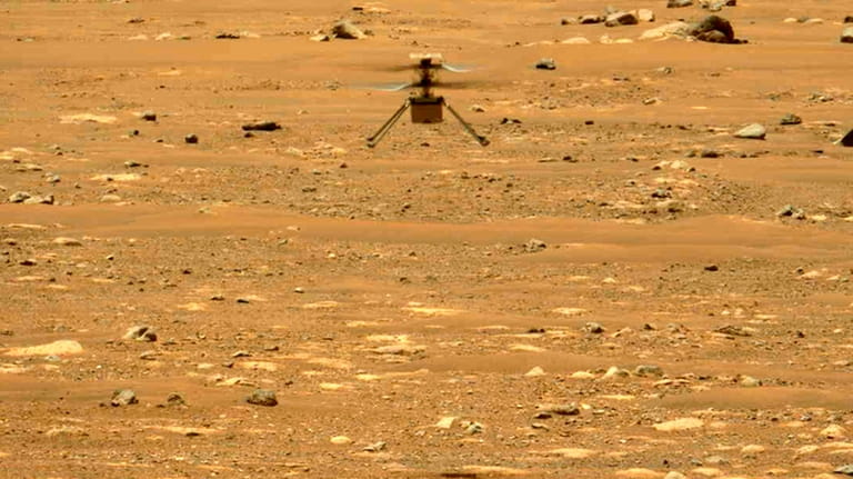 The Mars Ingenuity helicopter hovers above the surface of the...