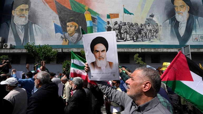 Iranian worshippers walk past a mural showing the late revolutionary...