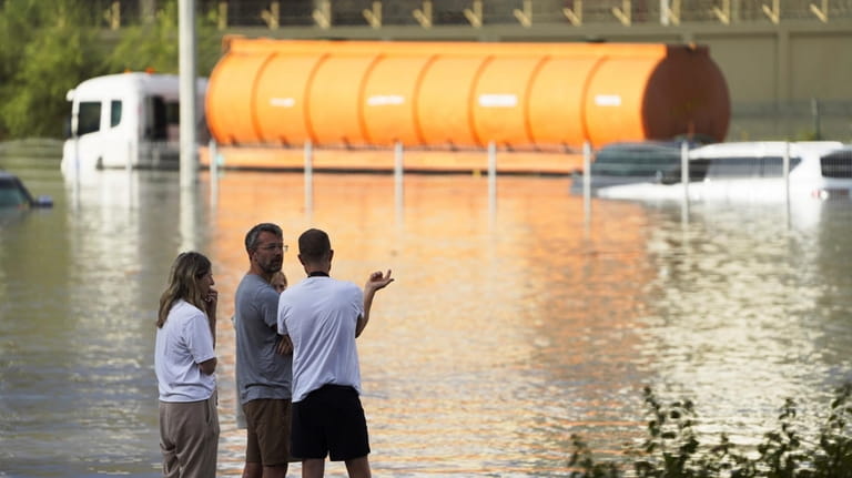People look out at floodwater covering a major road in...