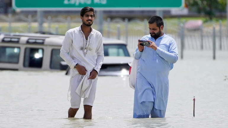 Two men walk through floodwater in Dubai, United Arab Emirates,...
