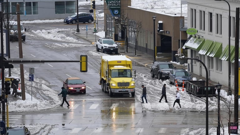 Pedestrians crosses the street as snow partially covers the roads,...