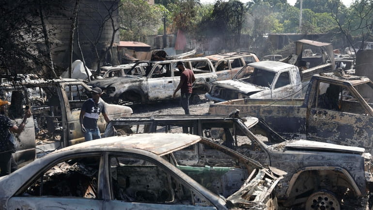 People look for salvageable pieces from burned cars at a...