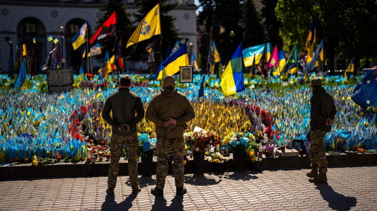 Ukrainian service men stand next to Ukrainian flags and photographs...
