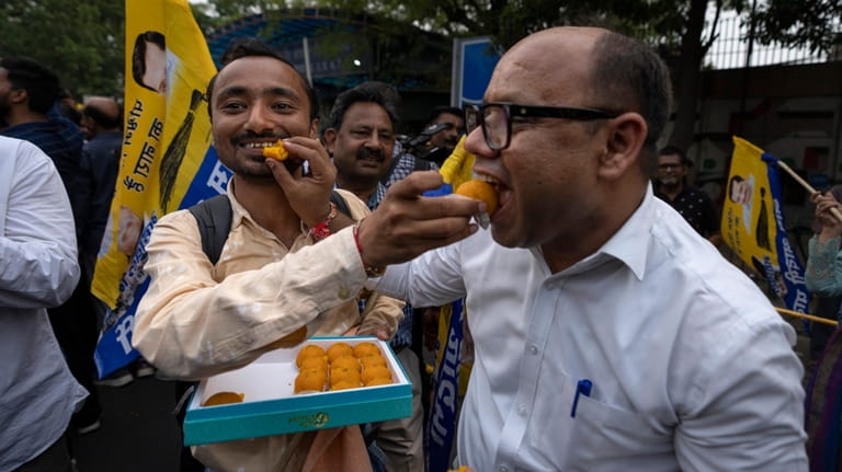 Supporters of the Aam Aadmi Party offer sweets to each...