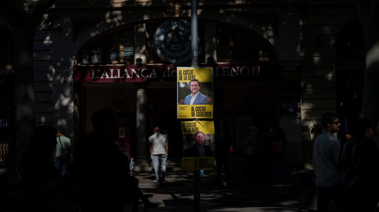 People walk past electoral posters showing a portrait of Catalan...