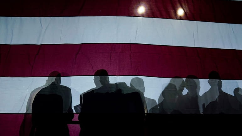Silhouettes of people are seen on an American flag as...