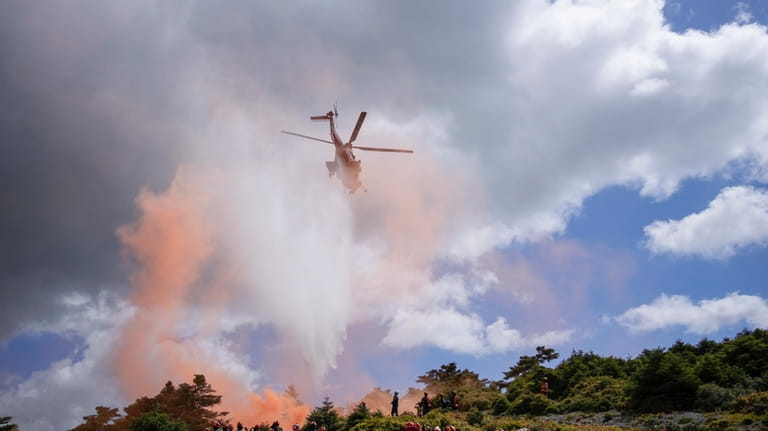 A helicopter drops water during a drill, as firefighters in...