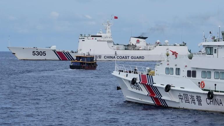 A Philippine supply boat, center, maneuvers around Chinese coast guard...