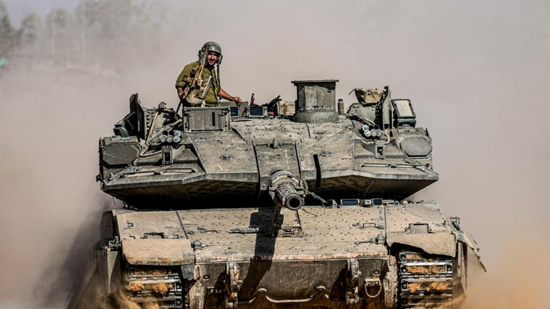 Israeli soldiers drive a tank at a staging ground near...