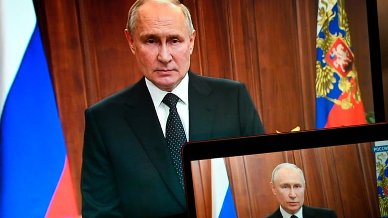Russian President Vladimir Putin is seen on monitors as he...
