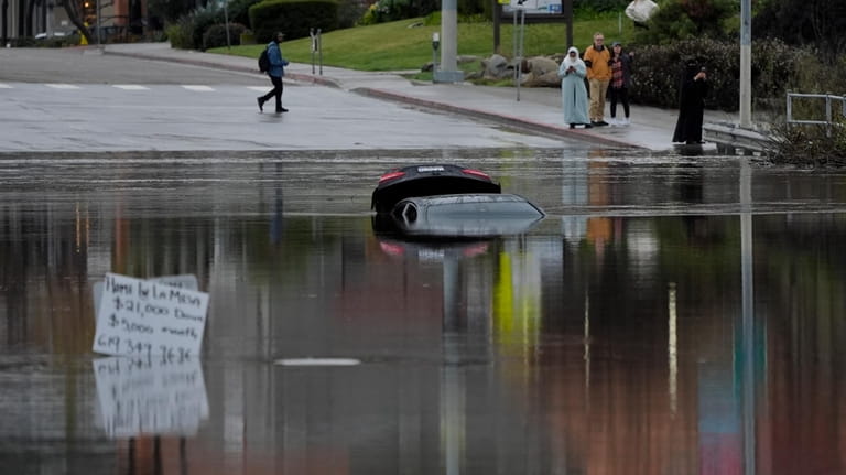 A car sits partially submerged on a flooded road during...