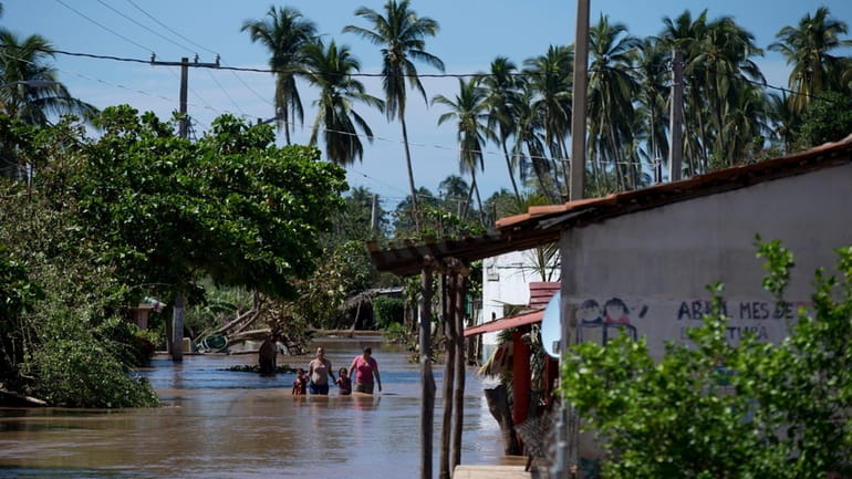 Residents wade down a street through receding floodwaters, two days...