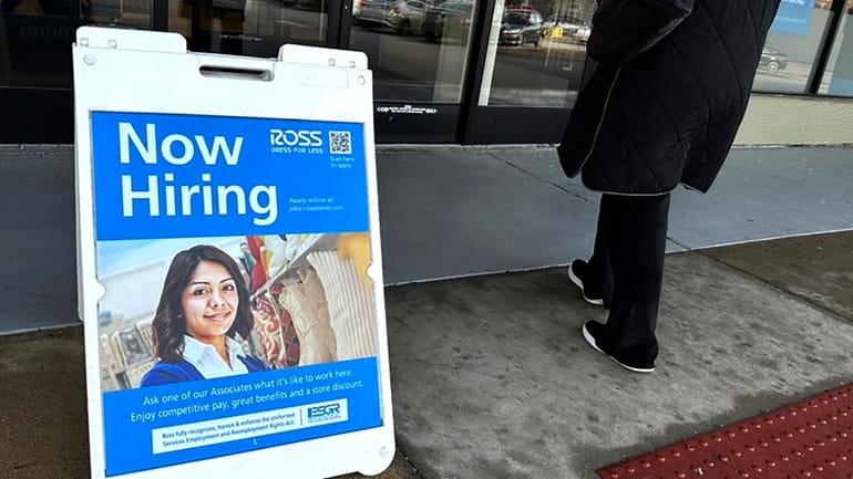 A hiring sign is displayed outside of a retail store...