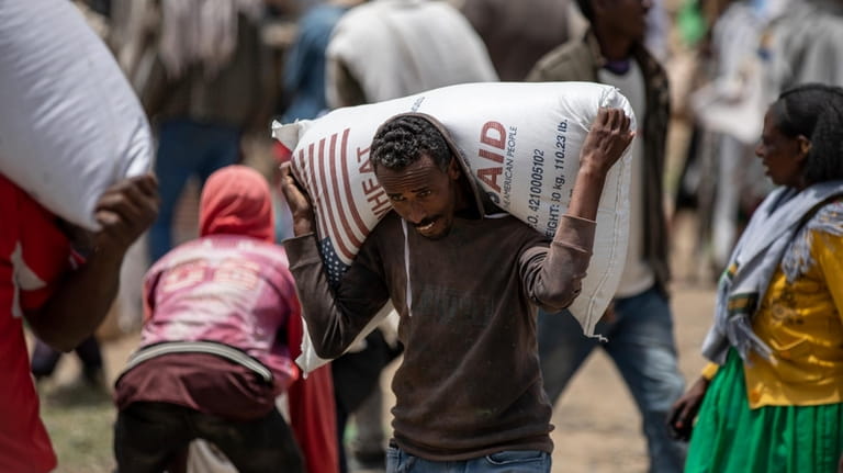 An Ethiopian man carries a sack of wheat on his...