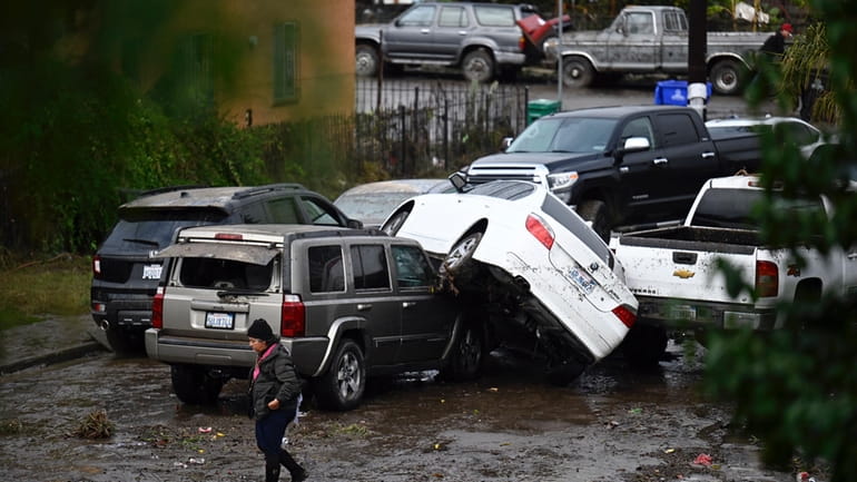 A woman walks by cars damaged from floods during a...