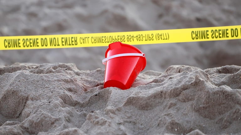 A pail rests next to caution tape on a beach...