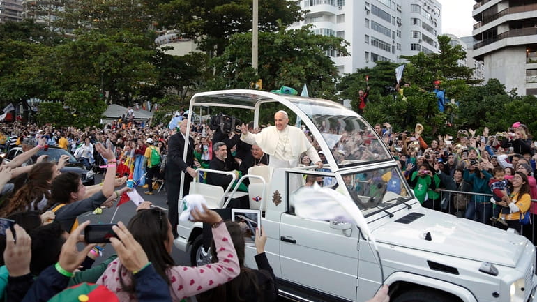 Pope Francis waves to people from his popemobile along the...
