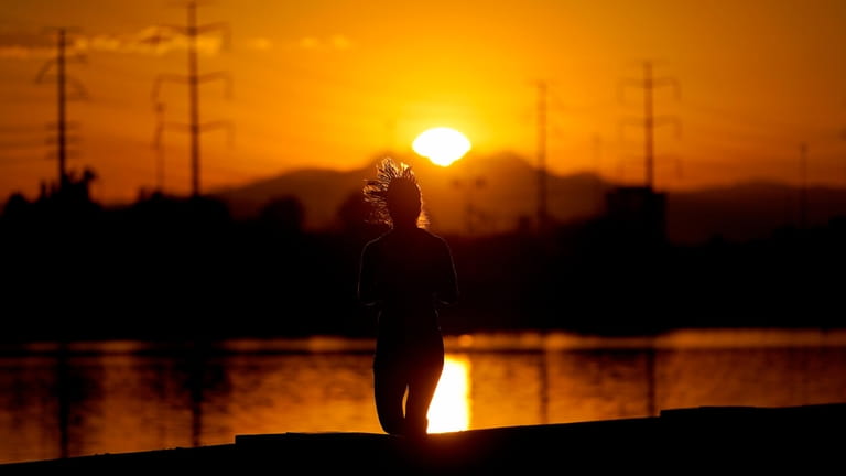 A runner jogs along Tempe Town Lake at sunrise, July...