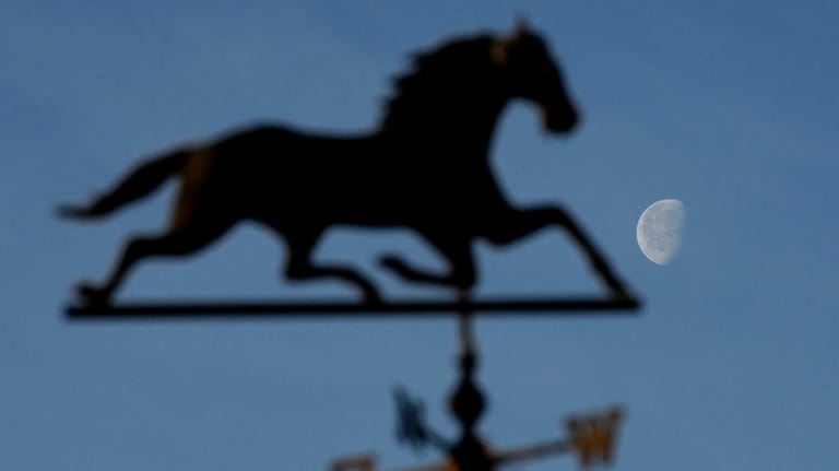 The moon rises beyond a weather vane on a barn...