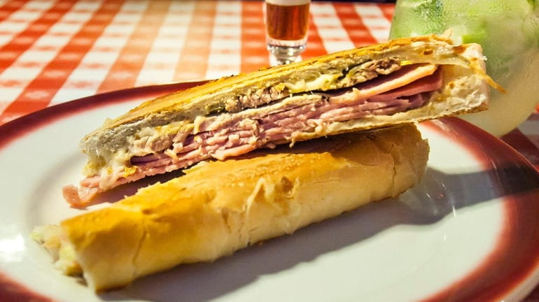 A Cuban sandwich with roasted pork, cooked ham, swiss cheese,...