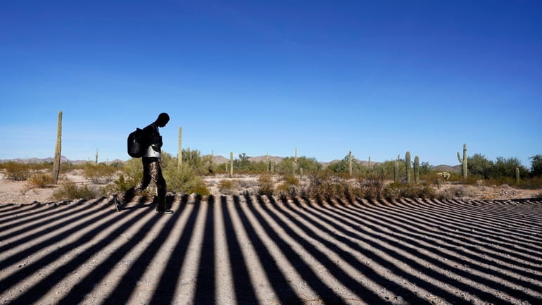 A migrant walks along a road shadowed by the steel...