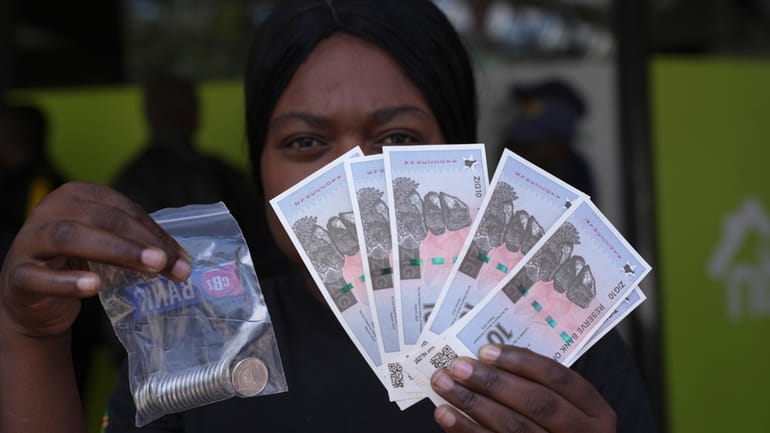 A woman holds the new Zimbabwean banknotes and coins called...