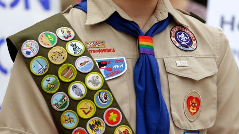 Merit badges and a rainbow-colored neckerchief slider are affixed on...