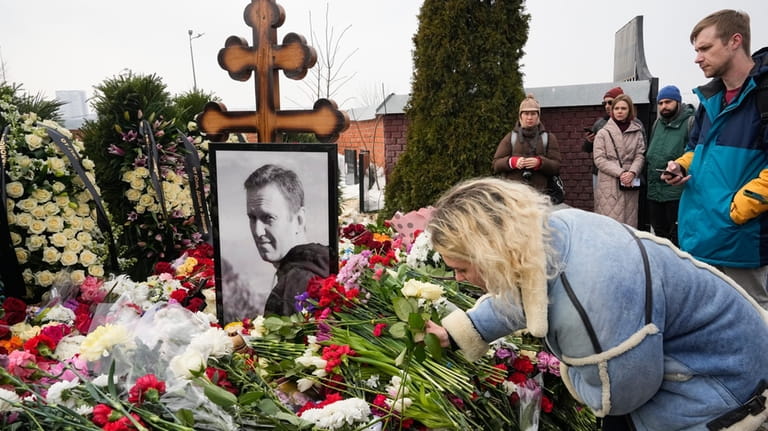 A woman lays flowers at the grave of Alexei Navalny...