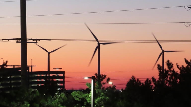 The sun sets behind spinning land-based wind turbines in Atlantic...